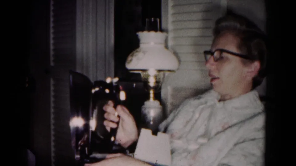 The woman appears pleased while holding the electric iron in a cozy Hagerstown living room, filmed on 8mm in 1958.