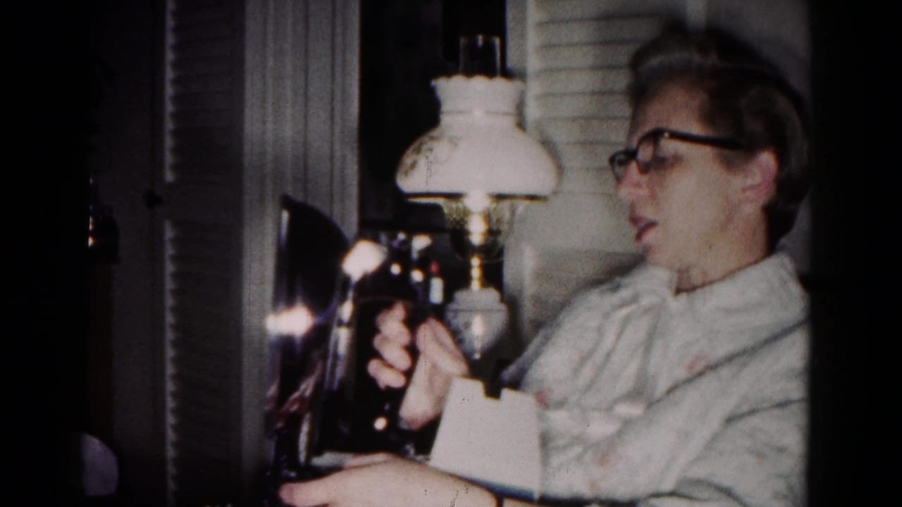 In a 1958 Hagerstown home interior, a woman in glasses holds a dark iron near a glowing lamp and curtains.