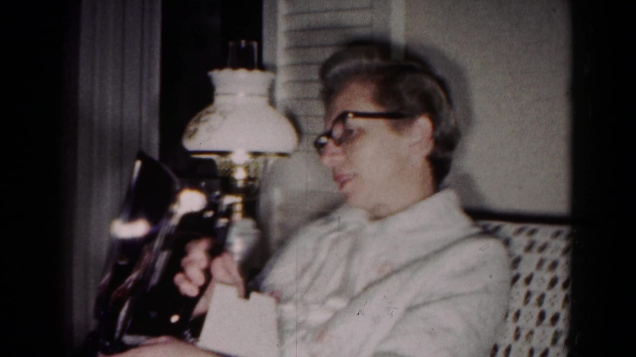 Woman in glasses looks down while holding a dark iron near a lamp.