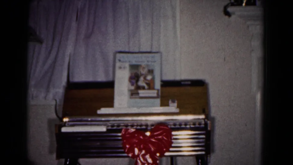 A wooden keyboard instrument stands below curtains, decorated with a large red bow and a music book on top.