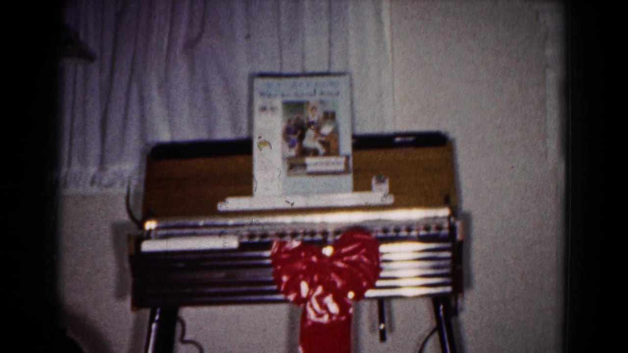 Small keyboard instrument with a red bow, music book, sheer curtain, and pale wall.