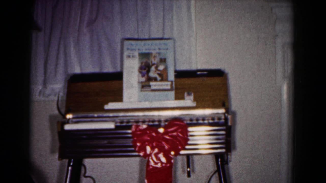 Small organ or piano with red bow, music book, curtain, and interior wall.