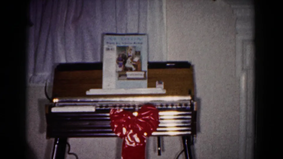 Final 1958 home-movie frame holds the small organ or piano with a red gift bow in a private Hagerstown interior.