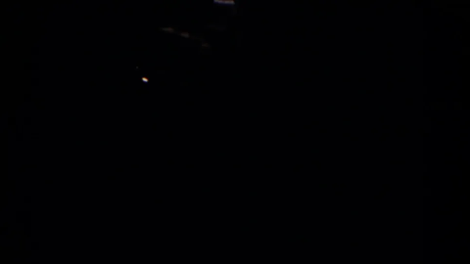 A mostly underexposed home-movie frame shows a dark interior transition with limited visible room detail.