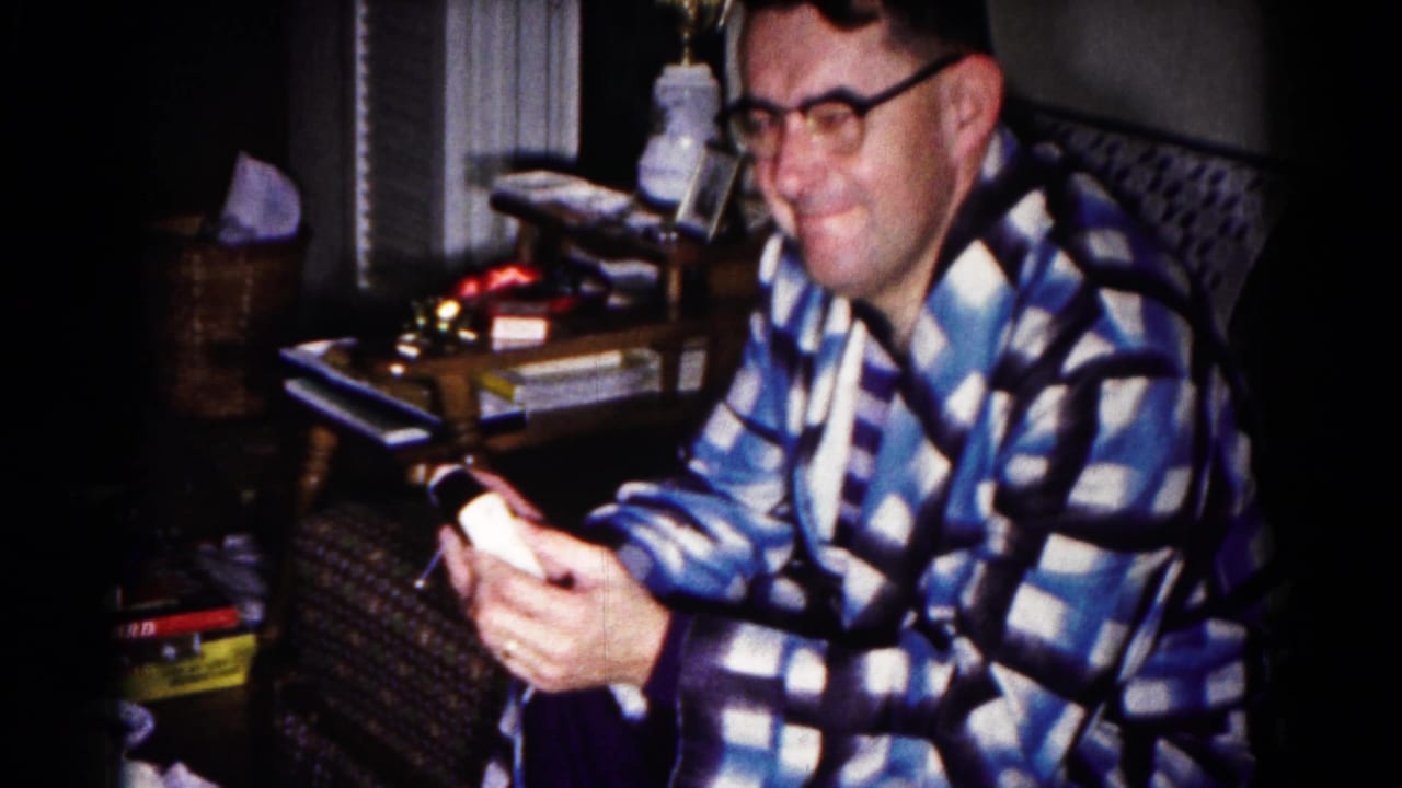 Man in a check robe smiles while holding a small device in both hands.