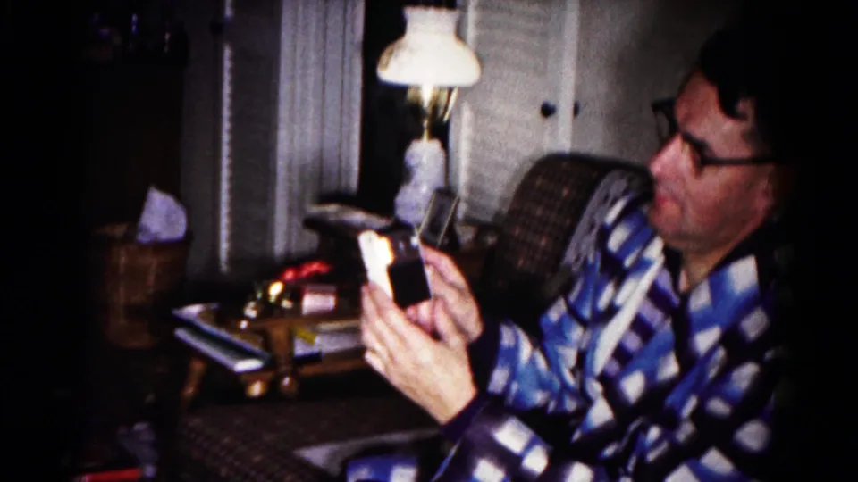 In the home-movie frame, the man tilts the small device toward himself while seated in a dim Hagerstown living room.
