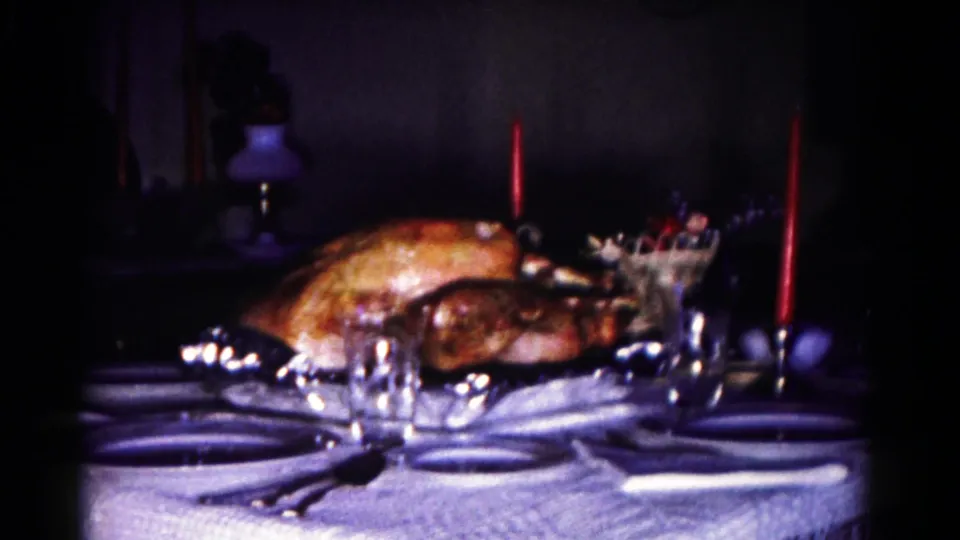 1958 Hagerstown dining table view with roasted turkey, place settings, clear glasses, and red candles in low light.
