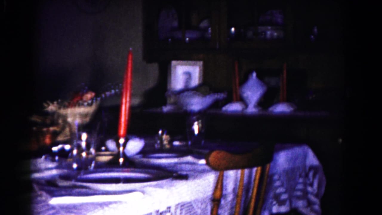 Dim dining table with lace tablecloth, red candles, place settings, and shelves in the background.