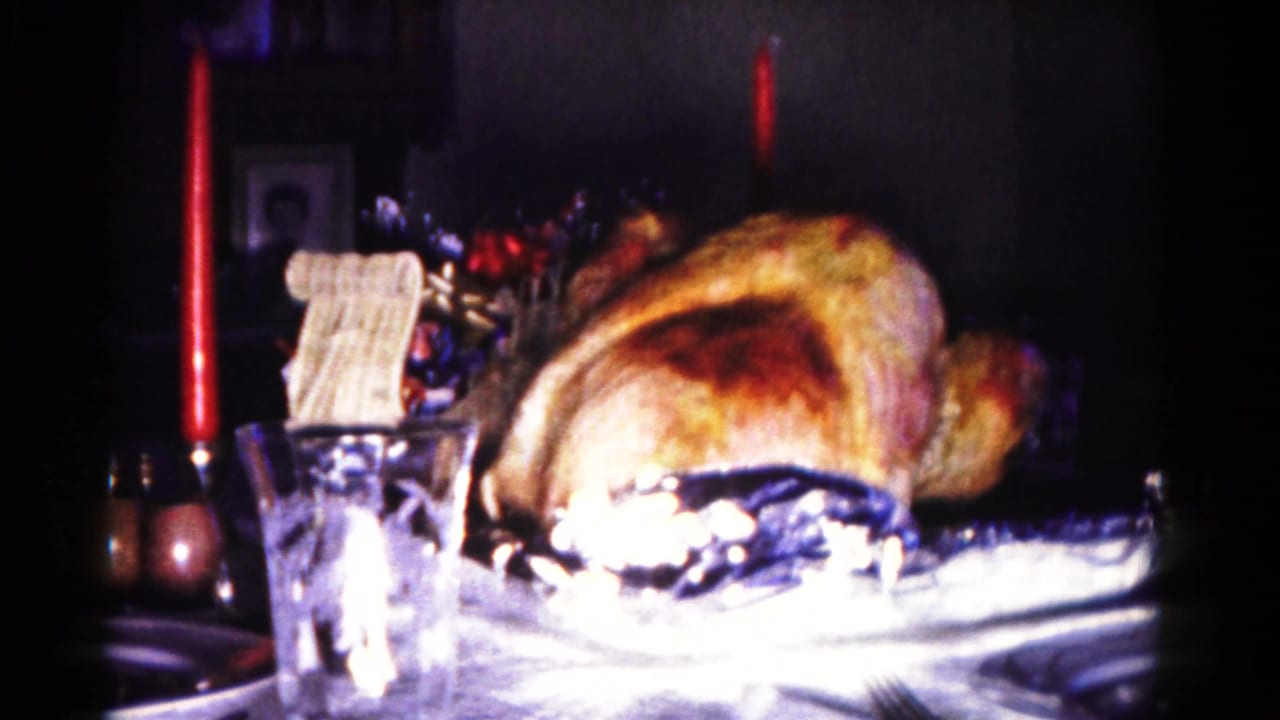 1958 Maryland home-movie frame centering a roasted turkey on a formal table with candles, glassware, and background decor.