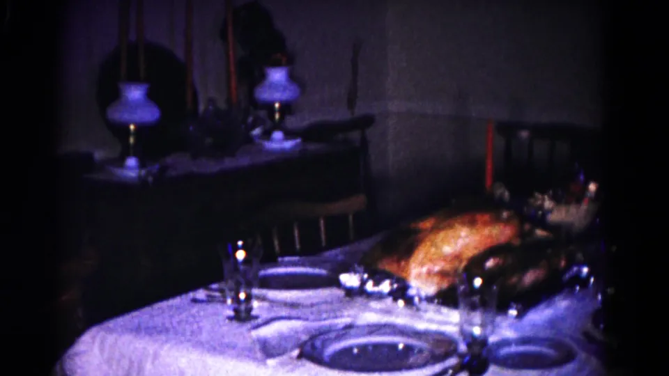 Wider 1958 Hagerstown home interior view showing the holiday table with turkey, place settings, glassware, chairs, and a lamp in dim light.