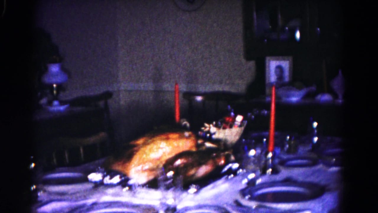 Dining table with turkey, dishes, glassware, red candles, chair, lamp, and portrait.