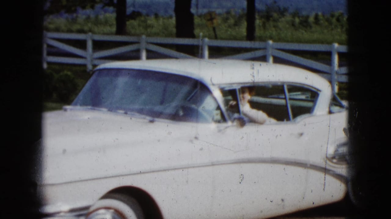 1958 Las Vegas home-movie frame showing a white vintage sedan by a white fence, with a woman partly visible inside.