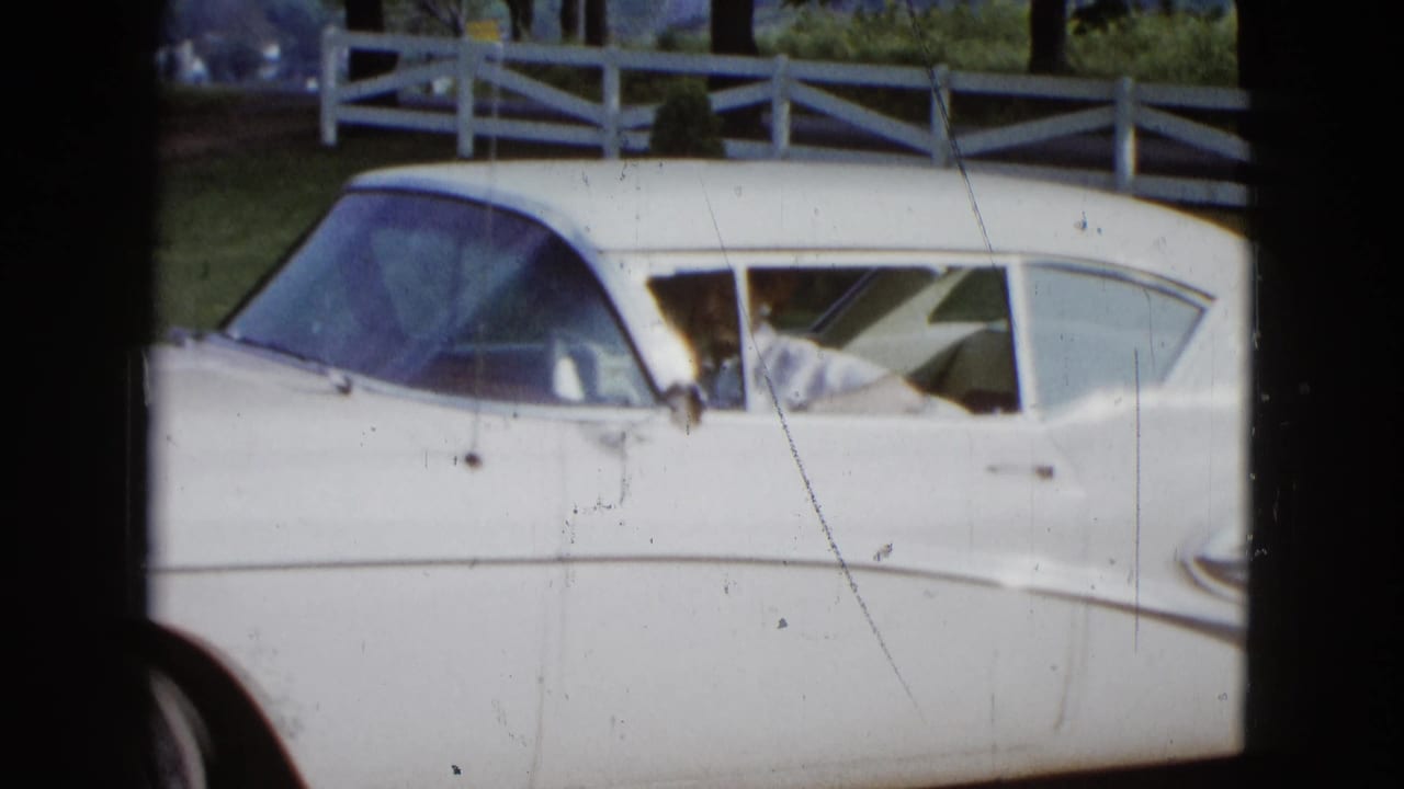 1958 Las Vegas frame of a white mid-century sedan near a fence, with a woman visible through the side window area.