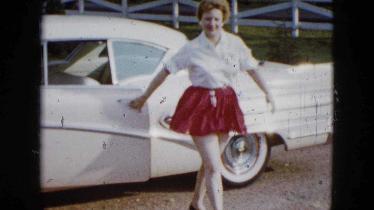 In 1958 Las Vegas home-movie footage, a woman in a red skirt and white blouse exits a white tail-fin car by a fence.