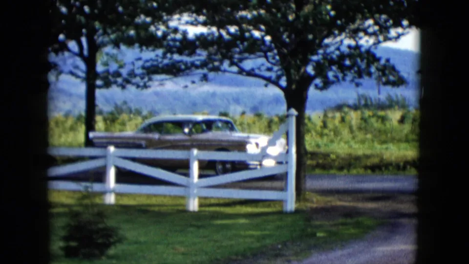 1958 home-movie frame of a two-tone sedan moving past a white fence in the Las Vegas, Nevada clip metadata setting.