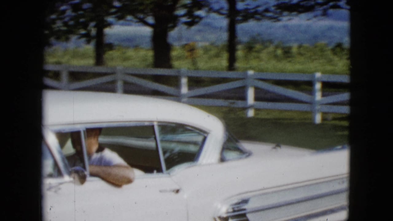 Man driving a white car with his arm resting in the open window.