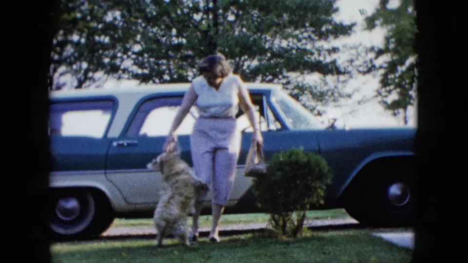 1958 Las Vegas home-movie frame showing a woman on a lawn with a small fluffy dog near a blue and white station wagon.