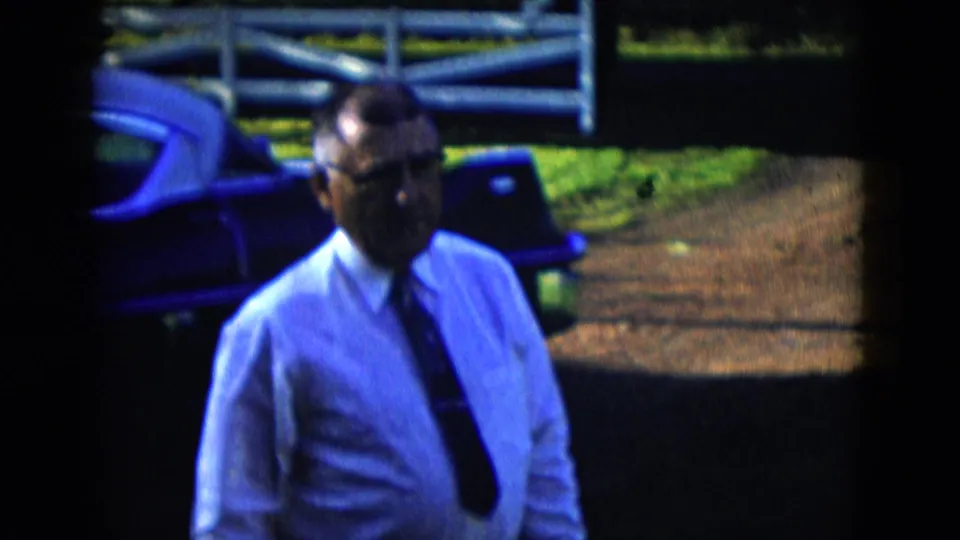 The clip ends with a closer view of the man in glasses walking beside the sedan, with a paved path and white fence in the Las Vegas-area setting.