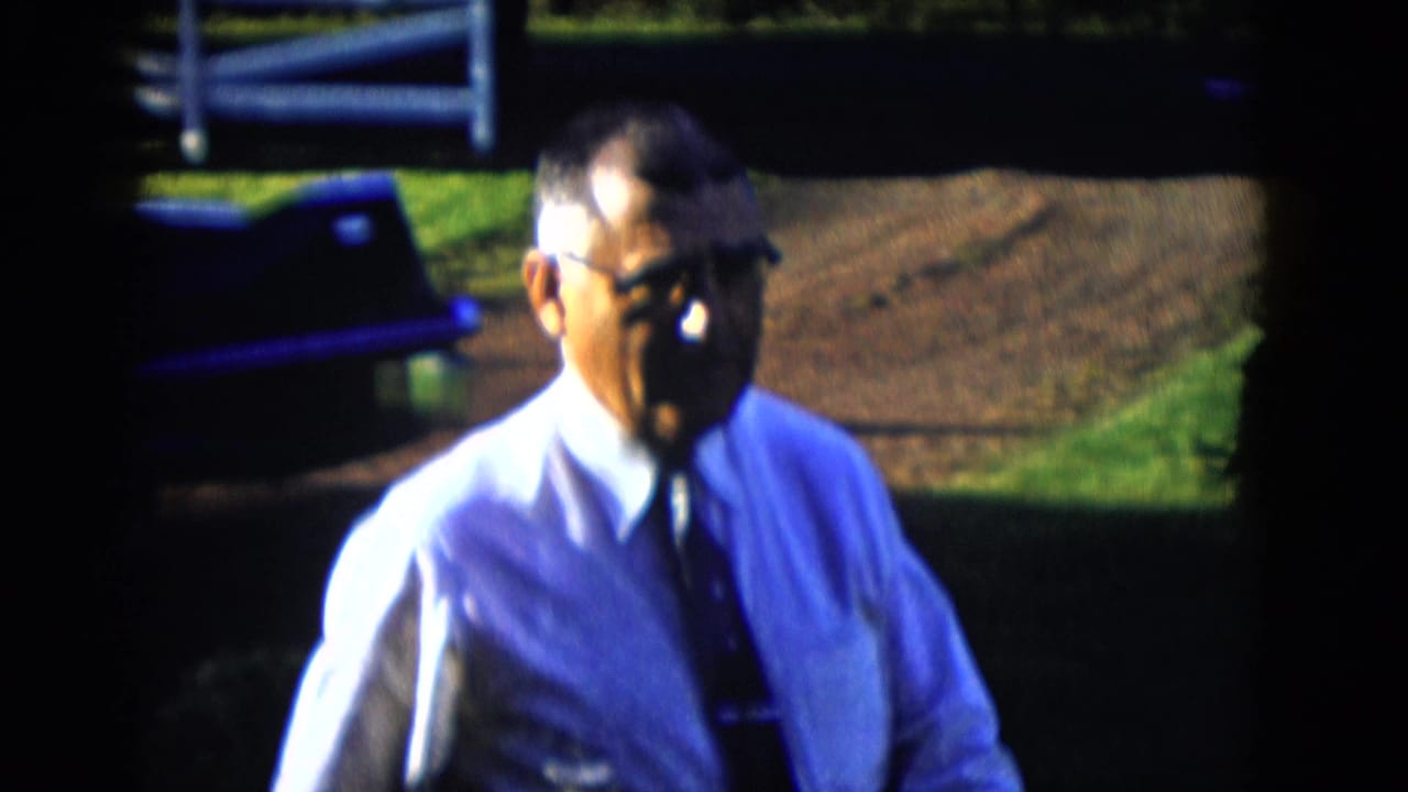 In 1958 Las Vegas-area home-movie footage, an older man in glasses and a light shirt stands near a dark car in bright sun.