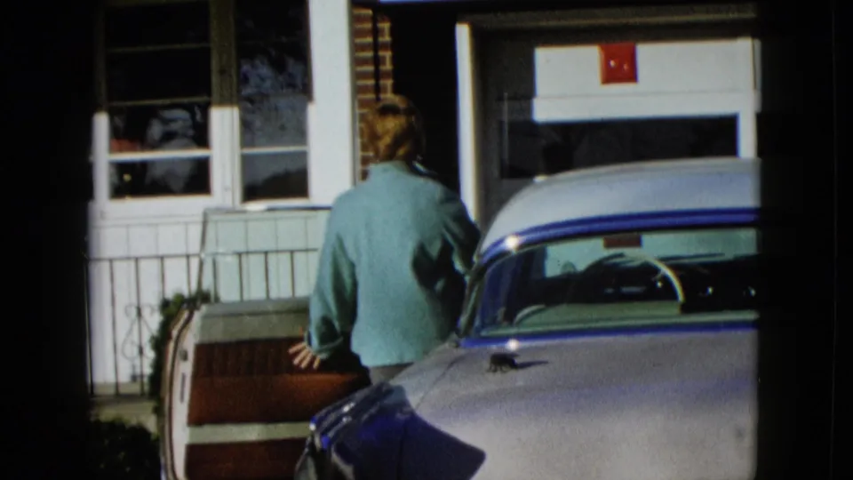 Seen from behind, the woman opens the car door next to the pale 1950s vehicle outside the Las Vegas residence described in the metadata.