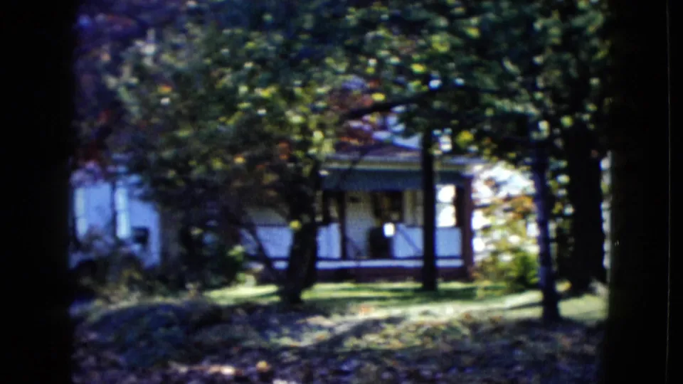1958 Las Vegas residential exterior partly screened by trees, with porch details and a shaded front yard visible.