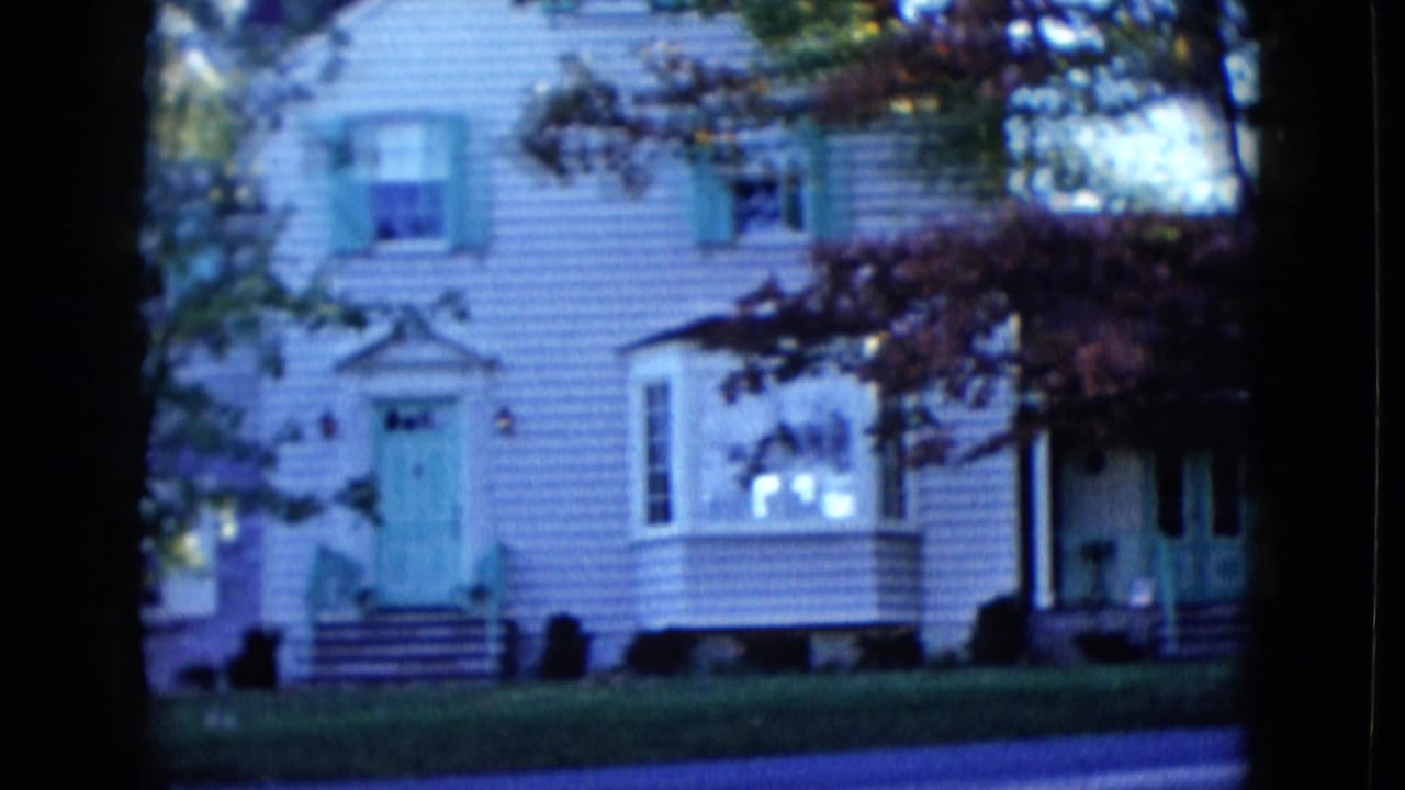 Light-colored house with green shutters, bay window, lawn, and trees near a quiet street.