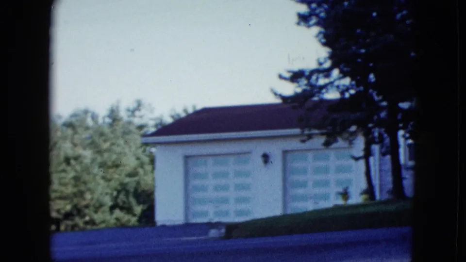 1958 Las Vegas suburban frame showing a two-car garage, pale doors, low roofline, trees, lawn, and street foreground.