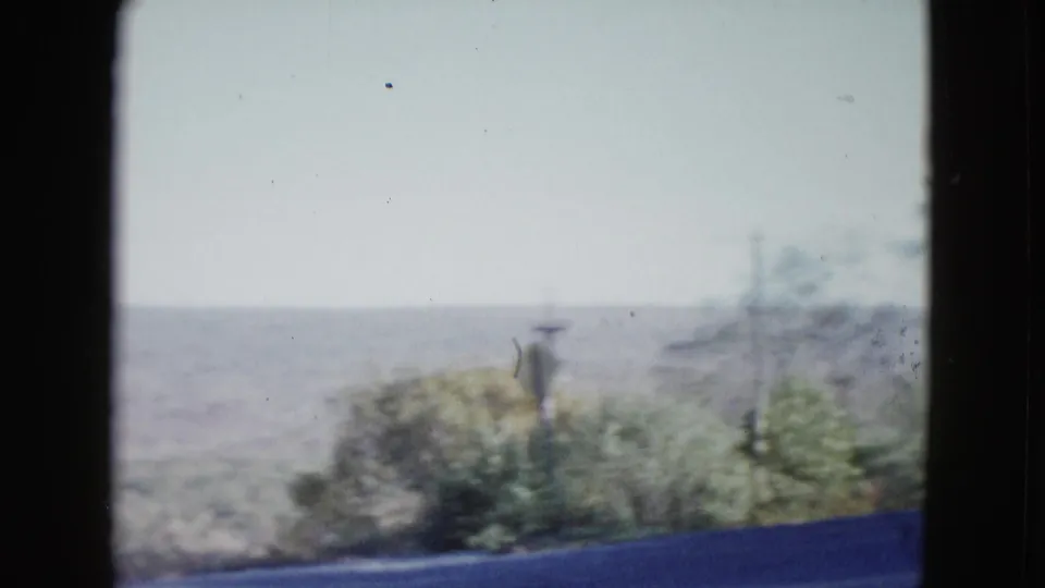 1958 Las Vegas-area roadside view with scattered desert shrubs, utility poles, distant hills, and soft 8mm exposure.