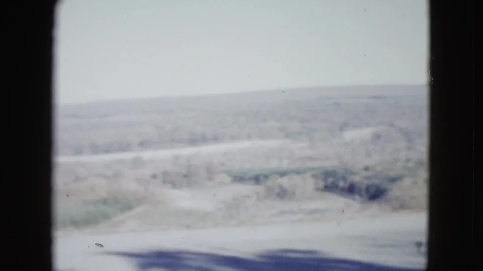 1958 Las Vegas-area frame showing a roadside slope, scrub brush, open desert ground, and a hazy horizon in faded 8mm color.