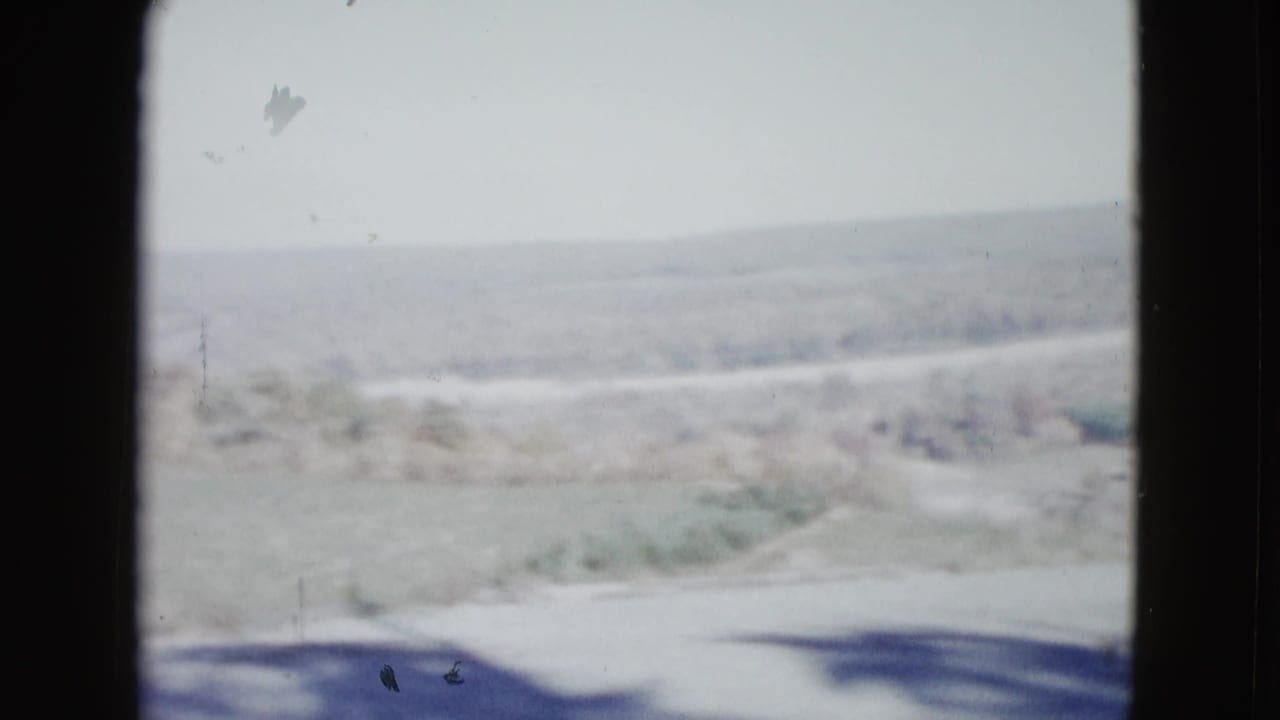1958 8mm home-movie frame of a rural landscape near Las Vegas, showing pale fields, distant hills, and dark scan borders.