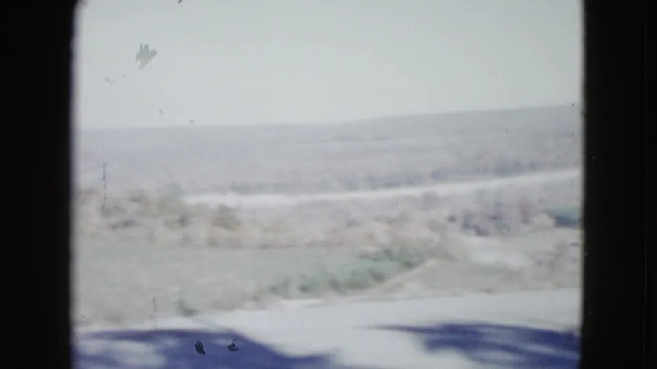 1958 8mm home-movie frame of a rural landscape near Las Vegas, showing pale fields, distant hills, and dark scan borders.