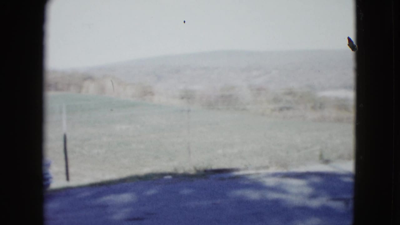 1958 rural Nevada roadside view with open field, distant hills, a dark pole, and shadowed pavement at the bottom of frame.