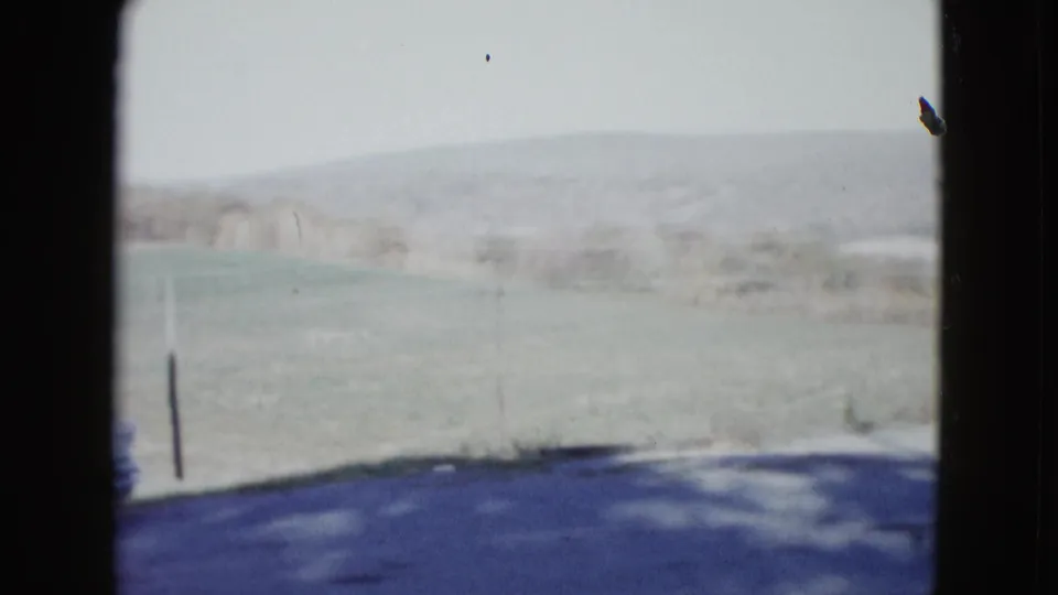1958 rural Nevada roadside view with open field, distant hills, a dark pole, and shadowed pavement at the bottom of frame.