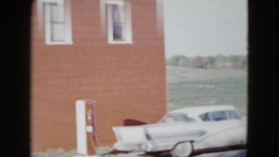 1958 8mm frame of a red roadside building near Las Vegas, with two windows, a gas pump, and a white finned sedan.