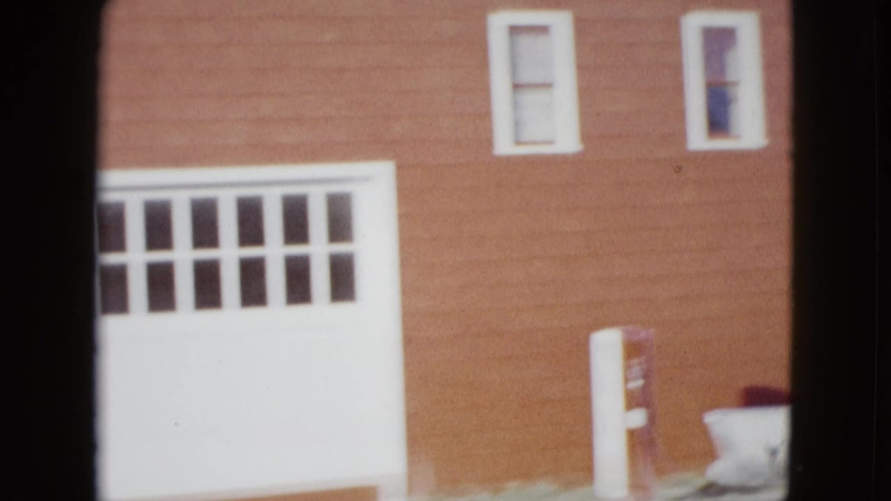 1958 Las Vegas home-movie frame showing a red-sided building with white trim, garage door, upper windows, and a gas pump in the yard.