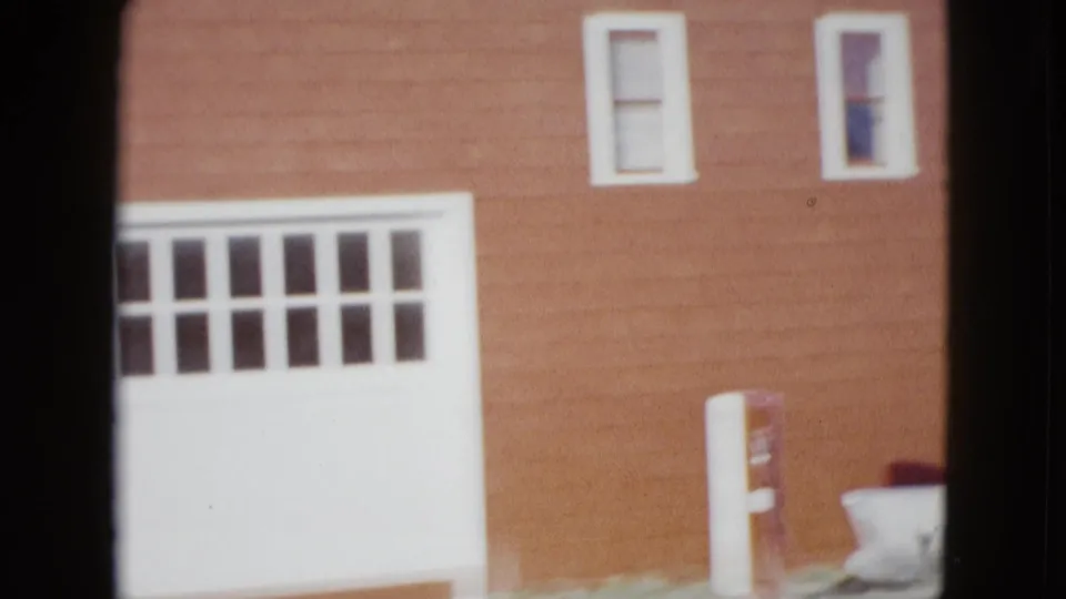 1958 Las Vegas home-movie frame showing a red-sided building with white trim, garage door, upper windows, and a gas pump in the yard.