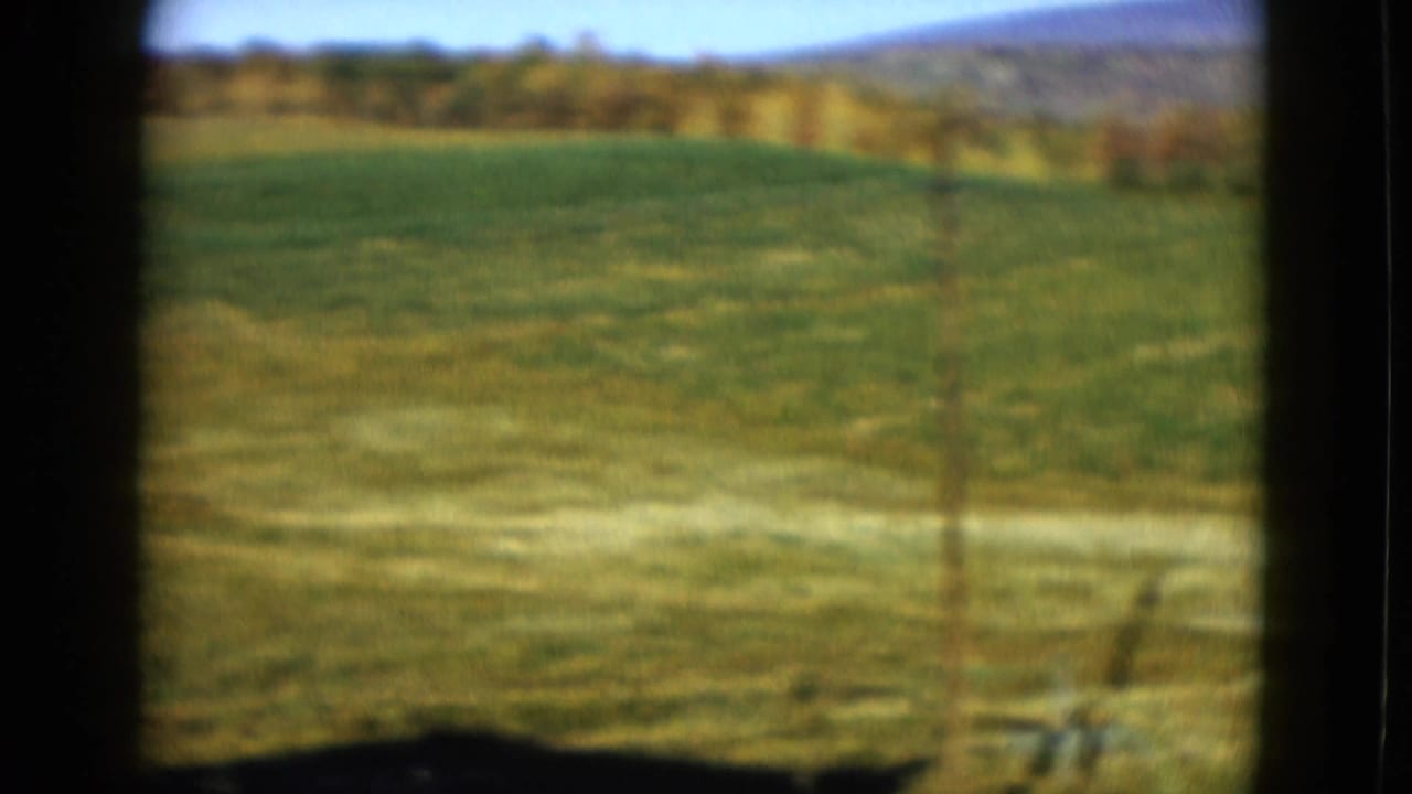 1958 8mm home-movie frame showing green farmland, distant tree line, and low hills in the Las Vegas metadata context.