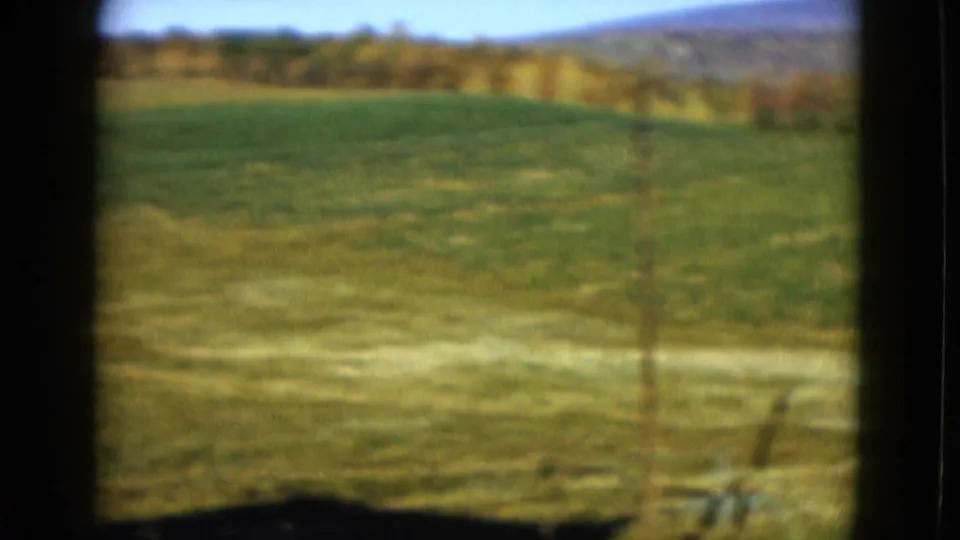 1958 8mm home-movie frame showing green farmland, distant tree line, and low hills in the Las Vegas metadata context.