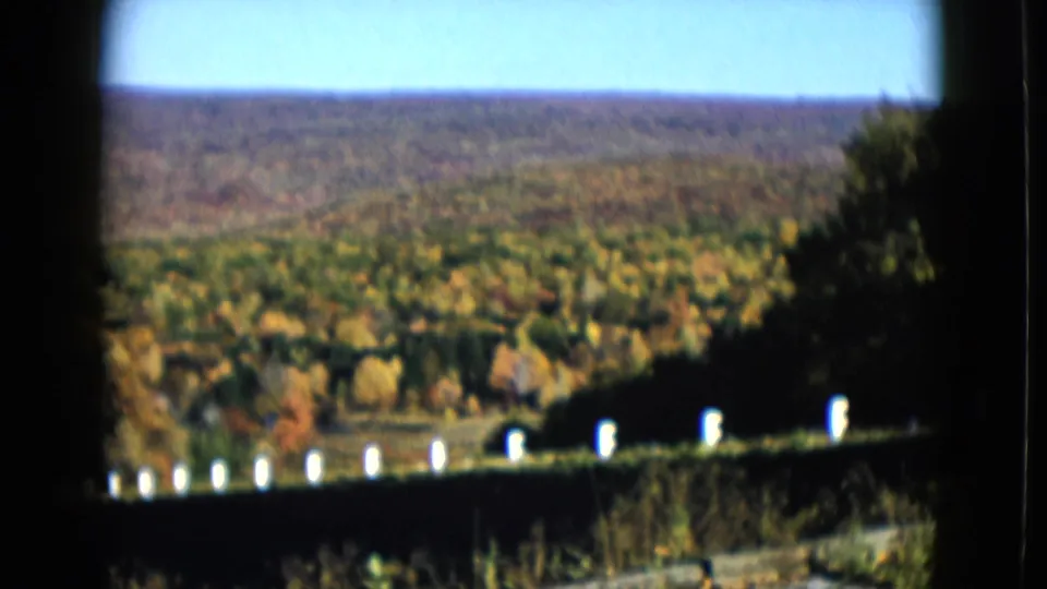 1958 8mm frame showing a white fence line along wooded rural terrain and distant hills in the Las Vegas metadata context.