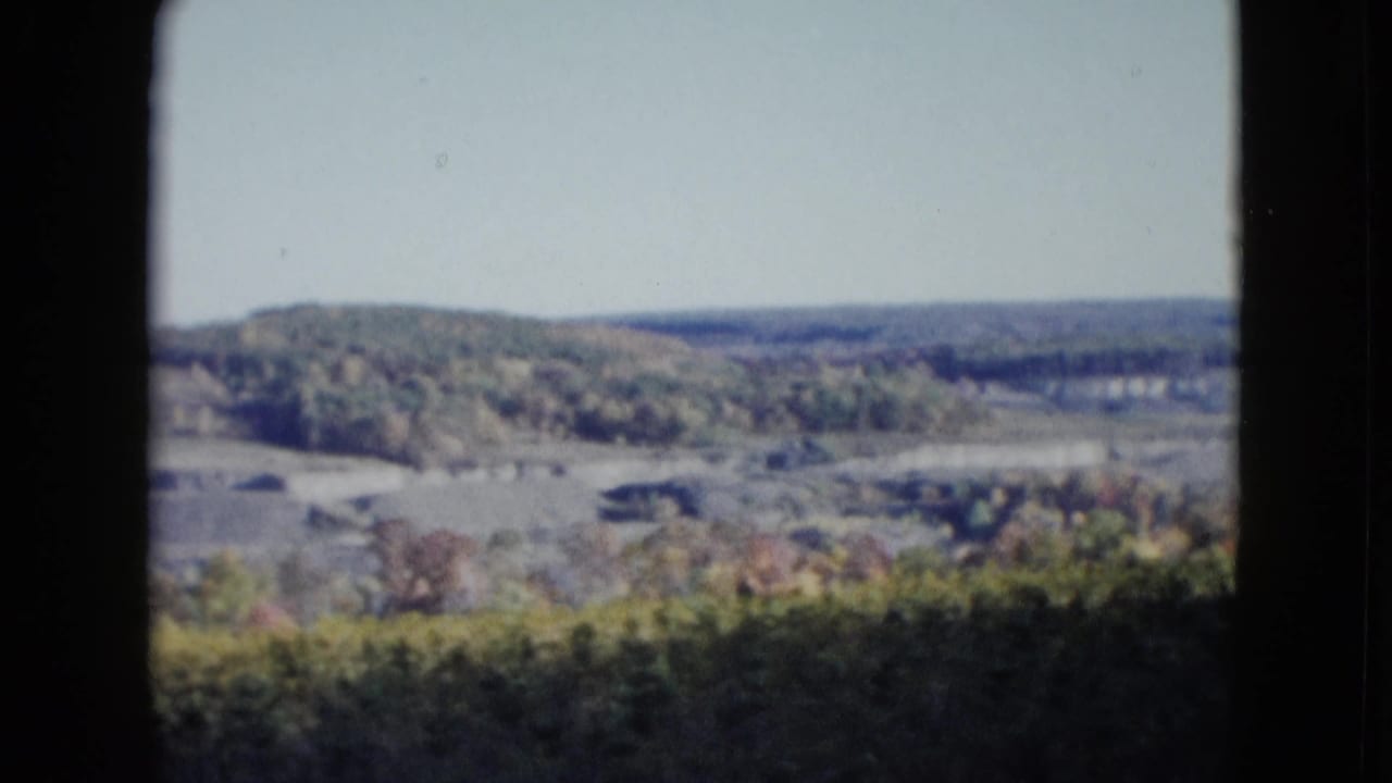 Elevated view of wooded hills, terraced earthworks, and autumn trees framed by dark film borders.