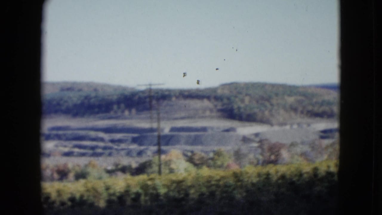Terraced hillside landscape with a utility pole, wooded ridge, pale sky, and dark frame edge.