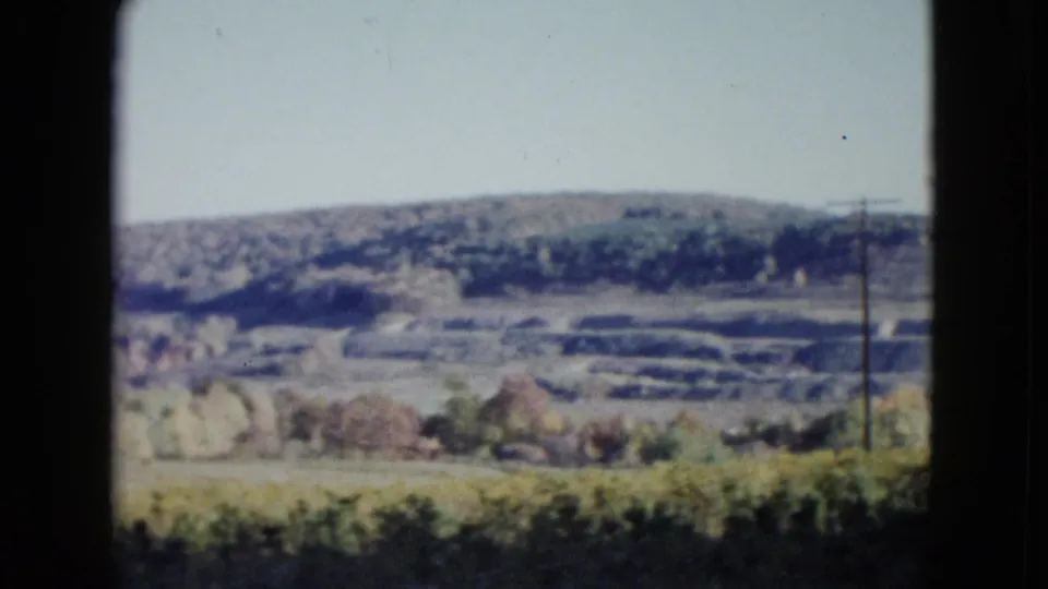 1958 Las Vegas-area 8mm frame with terraced ground, a utility pole, autumn trees, and soft distant hills.