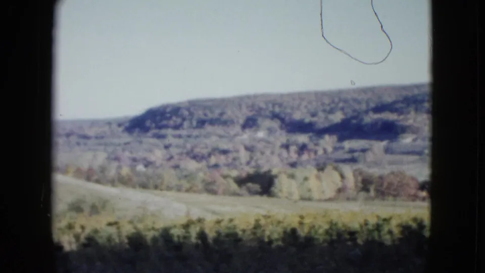1958 Las Vegas-area 8mm frame showing open hillside terrain and autumn trees with visible physical-film hair and grain.