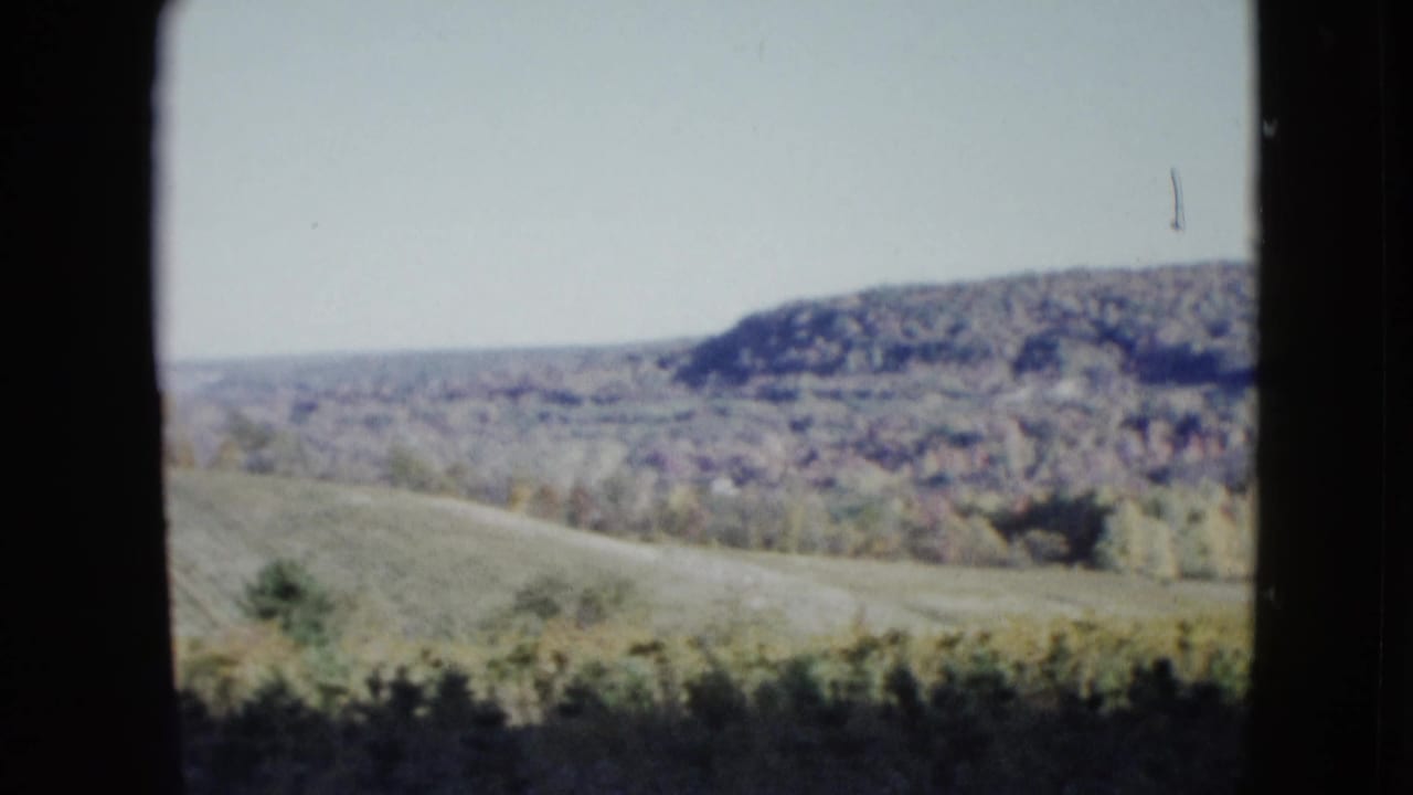 Rolling hills and open fields seen through dark window-like framing.