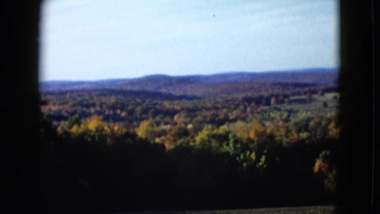 Wide 8mm frame of autumn trees and low hills, with the landscape partly enclosed by dark viewfinder-like edges.