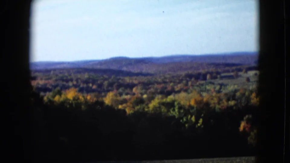 Wide 8mm frame of autumn trees and low hills, with the landscape partly enclosed by dark viewfinder-like edges.