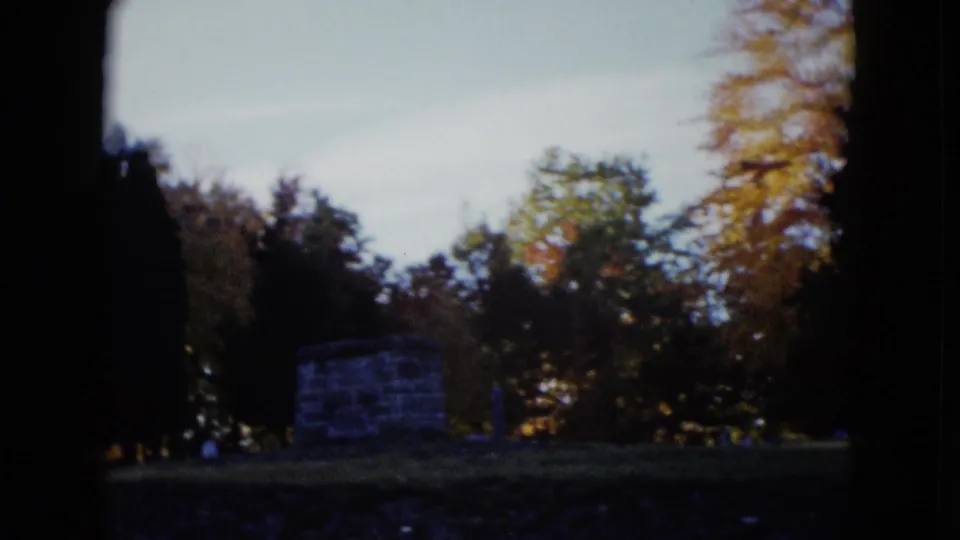 1958 Las Vegas home-movie frame showing grass, trees, and a small stone or masonry structure beyond the shaded foreground.