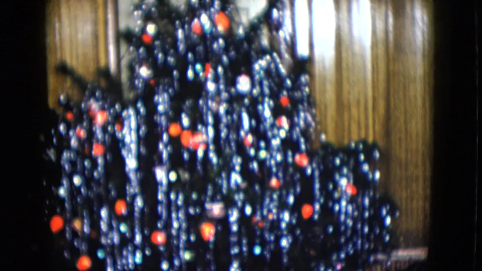 1958 Las Vegas home-movie frame showing a dark Christmas tree covered with silver tinsel and red ornaments.