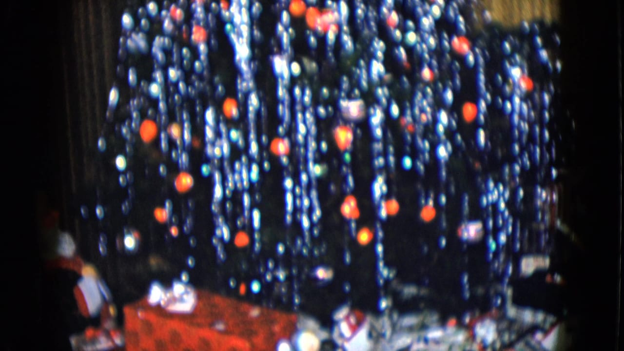 1958 Las Vegas interior view of a decorated Christmas tree with red ornaments, tinsel, presents, and small holiday figures below.