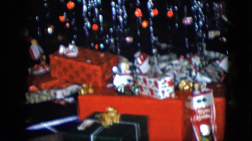 1958 Las Vegas home-movie frame showing a cluster of wrapped gifts below a tinsel-heavy Christmas tree in a private interior.